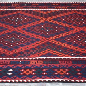 May include: A red, blue, and white patterned rug with a geometric design. The rug has a dark blue border with a repeating pattern.