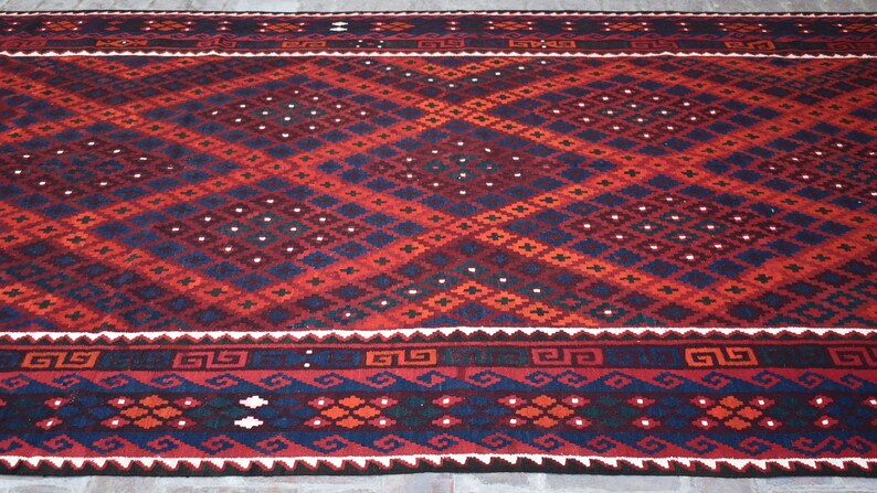 May include: A red, blue, and white patterned rug with a geometric design. The rug has a dark blue border with a repeating pattern.