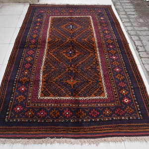 Può includere: Un tappeto persiano tradizionale con sfondo blu scuro e intricati motivi geometrici in tonalità di arancione, rosso e bianco. Il tappeto ha un bordo a frange.