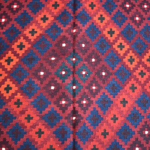 May include: A red, blue, and black patterned rug with a geometric design. The rug has a repeating pattern of squares and diamonds.