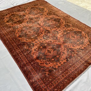 May include: A rectangular, hand-knotted rug with a detailed, repeating pattern in shades of rust, brown, and black. The rug features a central medallion design and a decorative border. The rug is likely made of wool and is suitable for a living room or bedroom.