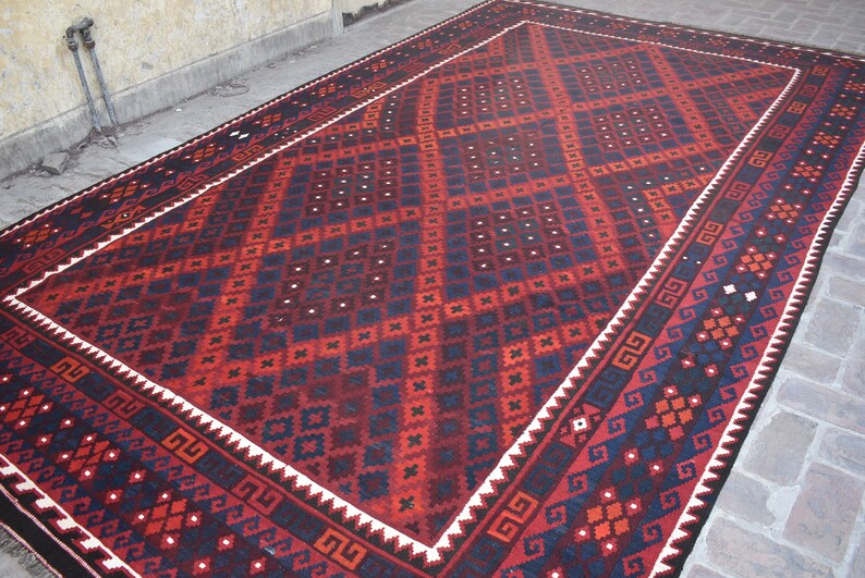 May include: A traditional red, black, and white patterned rug with a geometric design. The rug has a white border with a black and white geometric pattern.