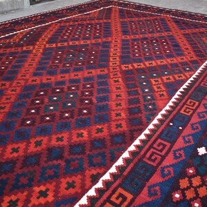 May include: A traditional red, blue, and white patterned rug with a geometric design. The rug has a white border with a repeating pattern.