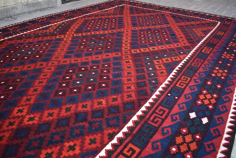 May include: A traditional red, blue, and white patterned rug with a geometric design. The rug has a white border with a repeating pattern.