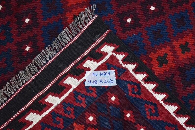 May include: Close-up of a red, blue, and white patterned rug with black fringe. A white tag with the text "No. 10213 4.18 X 2.50" is attached to the rug.