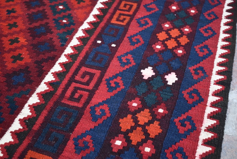May include: A close-up of a red, blue, and white patterned rug with intricate geometric designs. The rug has a traditional, hand-woven look.