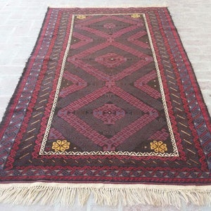 Pode incluir: Um tapete turco tradicional com fundo castanho escuro e padrões geométricos intrincados em tons de vermelho, roxo e dourado. O tapete tem uma borda de franjas.