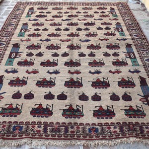 May include: A beige rug with a repeating pattern of stylized tanks and a border of red, blue, and white. The rug has a fringe edge.