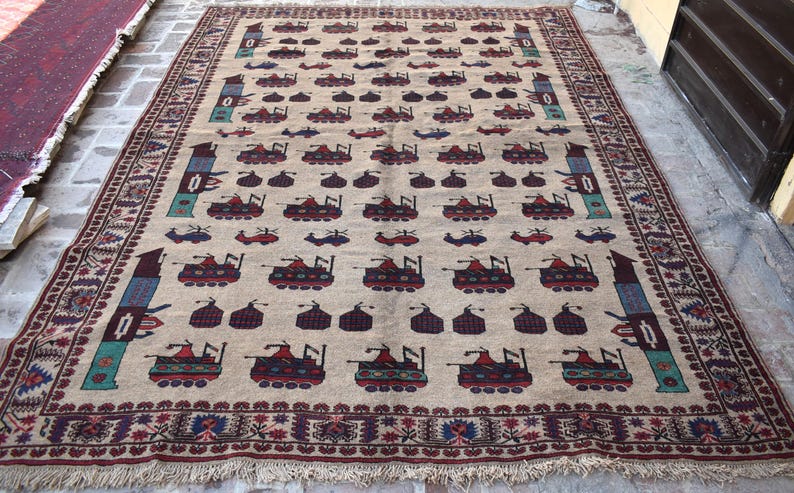 May include: A beige rug with a repeating pattern of stylized tanks and a border of red, blue, and white. The rug has a fringe edge.