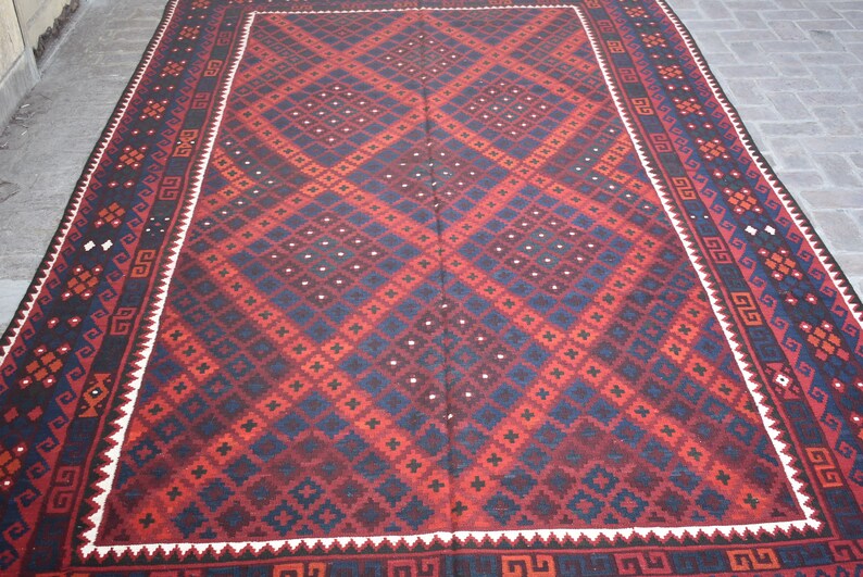May include: A traditional red, blue, and white patterned rug with a geometric design. The rug has a white border with a black and white geometric pattern.
