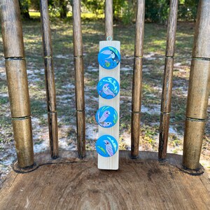 May include: A wooden plaque with four round, colorful buttons featuring different bird illustrations. The buttons are attached to the plaque with a metal pin. The plaque is hanging on a wooden chair.