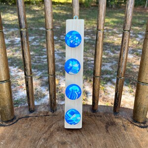 May include: A wooden block with four round blue and white painted magnets featuring sea life designs. The designs include a turtle, a seahorse, a jellyfish, and a crab.