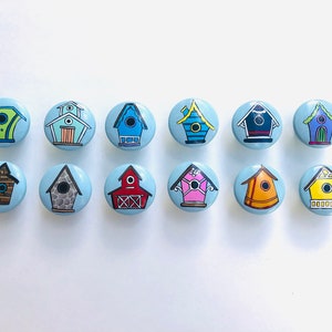 May include: Twelve different birdhouse designs painted on round blue ceramic knobs. Each knob features a unique birdhouse design with various colors and patterns.