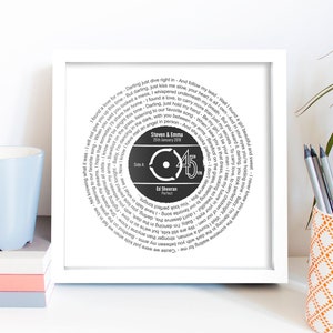 May include: A white framed print with a black and white circular design featuring the lyrics to the song "Perfect" by Ed Sheeran. The center of the design features a black circle with the number "45" and the text "Steven & Emma 25th January 2018".