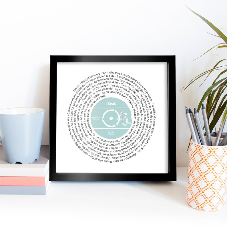 May include: A framed print of a record with the lyrics to the Oasis song "Live Forever" printed in a circle around the record label. The record label is light blue with the band name "Oasis" and the number "45" printed on it.