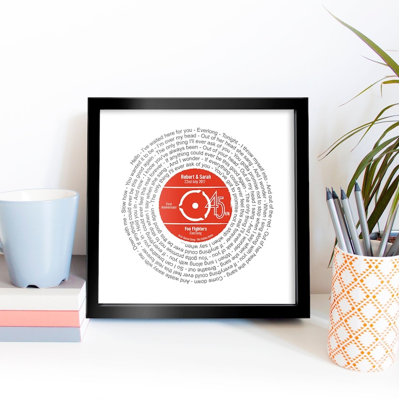 May include: A black framed print with a red and white record design. The record features the song "Everlong" by the Foo Fighters. The text "Robert & Sarah 22nd July 2017" is printed on the record.