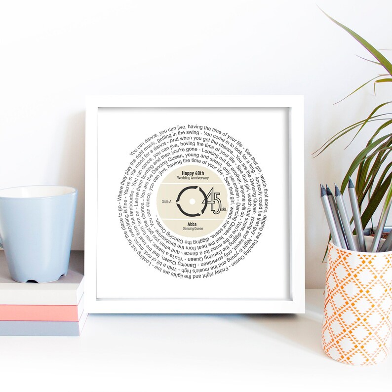May include: A white framed print with a beige background featuring a circular design of song lyrics from the song "Dancing Queen" by ABBA. The center of the circle features a record label with the number 45 and the text "Happy 45th Wedding Anniversary".