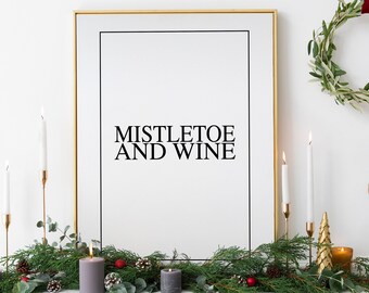 Könnte beinhalten: Ein goldfarbener gerahmter Druck mit dem Text "Mistletoe and Wine" auf weißem Hintergrund. Der Druck ist von einem Kranz aus Grün mit roten Beeren und Tannenzapfen umgeben. Auf dem Kaminsims stehen Kerzen und goldene Ornamente.