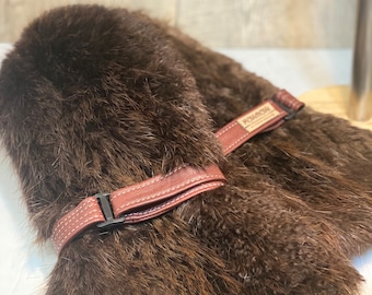 May include: A brown fur hat with a brown leather strap and buckle. The strap has the word "MASCHMANN" printed on it.