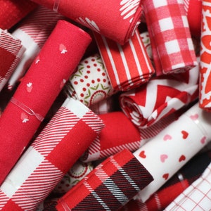 May include: A collection of red and white fabric scraps rolled up and tied with string. The fabrics feature various patterns including gingham, polka dots, hearts, and geometric designs.