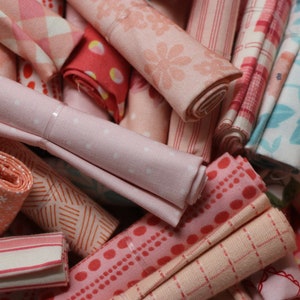 May include: A collection of fabric scraps in various shades of pink and orange with different patterns, including polka dots, stripes, and floral designs.