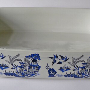 May include: White ceramic baking dish with a blue and white willow pattern. The pattern features birds, trees, and a pagoda.