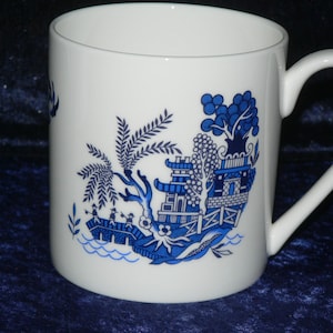 May include: White ceramic mug with a blue and white willow pattern. The pattern features a pagoda, a bridge, and a willow tree.