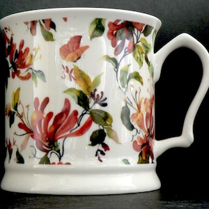May include: White ceramic mug with a floral design featuring red, orange, and yellow honeysuckle flowers and green leaves.