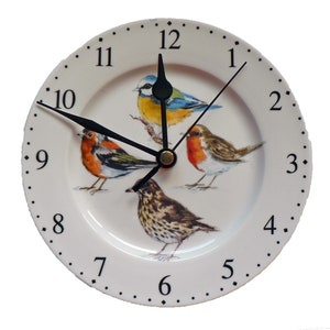 Pu&ograve; includere: Un orologio in ceramica bianca con lancette nere e numeri romani per le ore. Il quadrante dell'orologio presenta un disegno di quattro uccelli: una cincia azzurra, un pettirosso, un tordo e un scricciolo. L'orologio ha un diametro di 30 cm.