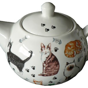May include: White ceramic teapot with a lid, featuring a whimsical design of cats and paw prints. The teapot has a rounded body and a spout on one side and a handle on the other.