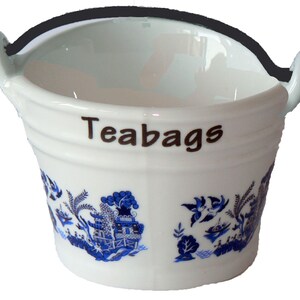 May include: White ceramic tea bag holder shaped like a bucket with a black handle. The bucket has a blue and white willow pattern and the word "Teabags" printed on the side.