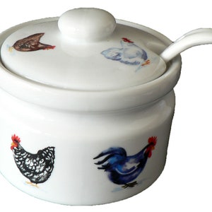 May include: White ceramic sugar bowl with a lid and a small spoon. The bowl features a chicken and rooster design with blue, black, white, and red accents.