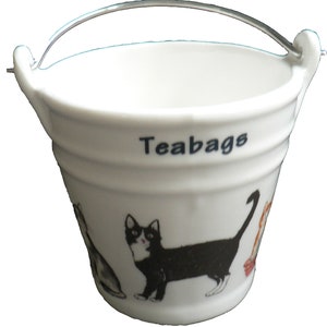 May include: White ceramic tea bag holder shaped like a bucket with a silver handle. The bucket has a black and white cat design and the word "Teabags" printed on the side.