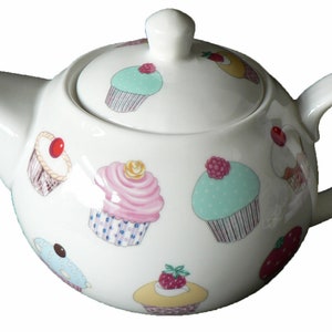 May include: White ceramic teapot with a lid, decorated with colourful cupcake illustrations. The teapot has a round body and a curved handle.