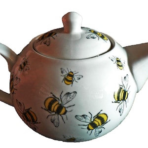 May include: White ceramic teapot with a lid, decorated with a pattern of yellow and black bees.