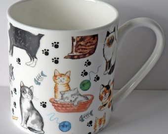 May include: White ceramic mug with a colorful cat pattern. The mug features various cats in different poses, including a black cat, a tabby cat, a Siamese cat, and a calico cat. The mug also has paw prints and fish bones printed on it.