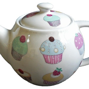 May include: White ceramic teapot decorated with colourful cupcake designs. The teapot has a curved spout, a rounded handle, and a lid with a small knob. The cupcakes are in shades of pink, blue, green, and yellow.