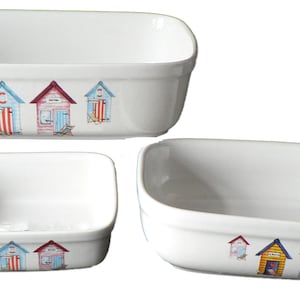 May include: Set of three white ceramic baking dishes with a beach hut design. The dishes are different sizes and feature a colourful illustration of beach huts with yellow, blue, red, and pink accents.