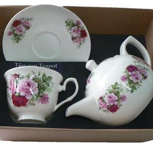 May include: A white porcelain tea set with a pink rose floral design. The set includes a teapot, a cup, and a saucer. The set is packaged in a brown box with the words "Two cup Teapot" printed on the box.
