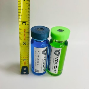 May include: Two glass vials, one with blue liquid and the other with green liquid, each with a colored cap. The vials are labeled "Compound V" and "Vought International". A yellow tape measure shows the vials are approximately 3 inches tall.