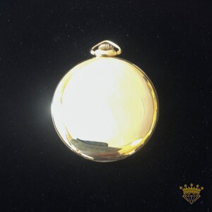 K&ouml;nnte beinhalten: Eine goldene Taschenuhr mit einem runden Geh&auml;use und einem schlichten Design. Die Uhr hat eine glatte, polierte Oberfl&auml;che und einen kleinen Knopf oben.