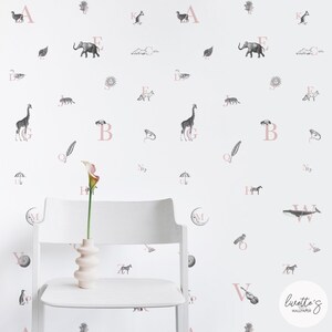 May include: A white wall featuring a pink alphabet and black and white illustrations of animals, objects, and nature. The letters are in a pink font and the illustrations are in a black and white style. The wall is decorated with a variety of illustrations, including a giraffe, an elephant, a whale, a bird, a frog, a feather, a moon, a sun, a cloud, an umbrella, a horse, a violin, and a penguin.