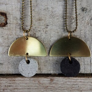 May include: Two gold necklaces with a half-circle pendant and a round pendant. One pendant is gray and the other is black.