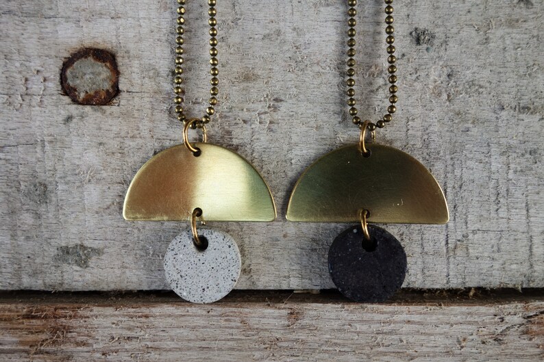 May include: Two gold necklaces with a half-circle pendant and a round pendant. One pendant is gray and the other is black.
