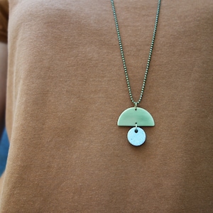 May include: A brass necklace with a half-circle pendant and a smaller round pendant. The necklace is on a brown shirt.