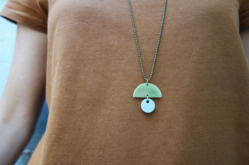 May include: A brass necklace with a half-circle pendant and a smaller round pendant. The necklace is on a brown shirt.