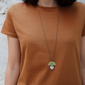 May include: A gold chain necklace with a green and white ceramic pendant. The pendant is a half circle shape with a smaller circle attached to the bottom.