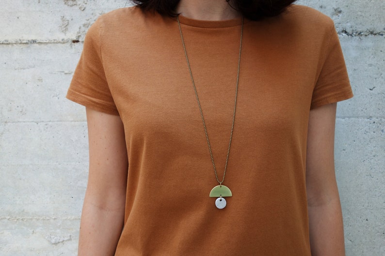 May include: A gold chain necklace with a green and white ceramic pendant. The pendant is a half circle shape with a smaller circle attached to the bottom.