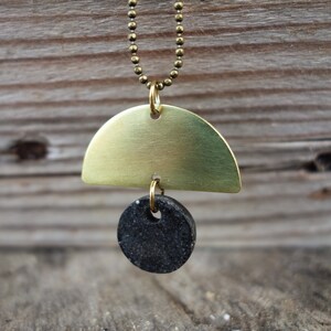 May include: A gold necklace with a brass half-circle pendant and a black round pendant.