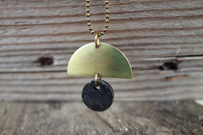 May include: A gold necklace with a brass half-circle pendant and a black round pendant.